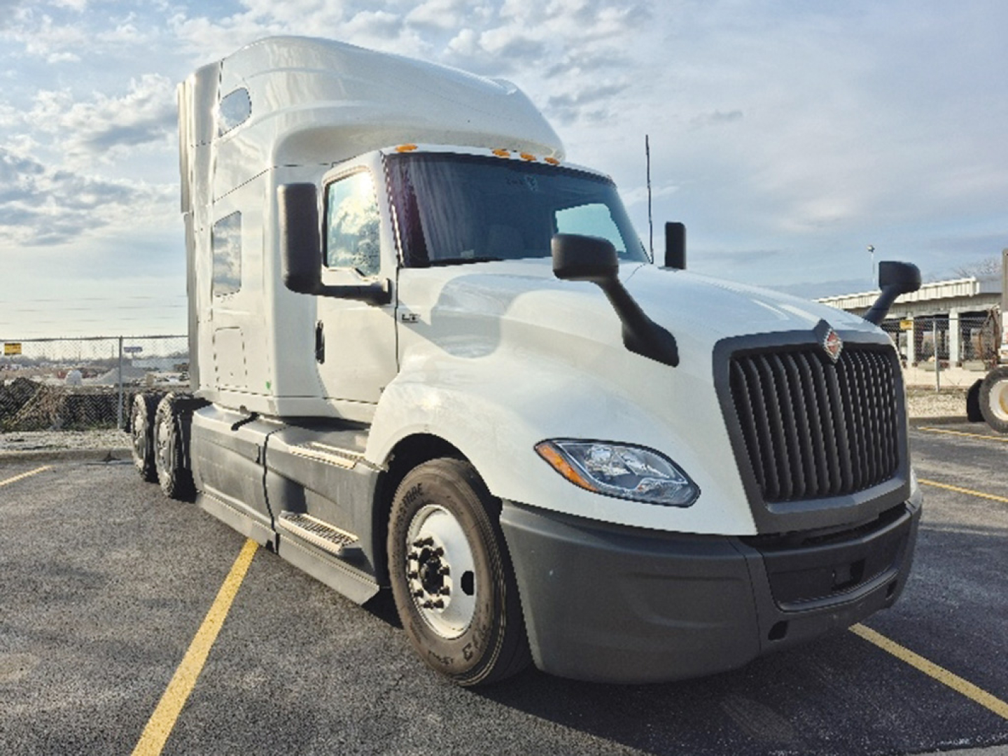 Truck cab and front view of a white 2023 International LT625 conventional sleeper semi-truck in a lot, showing grille, headlights, and side mirrors.