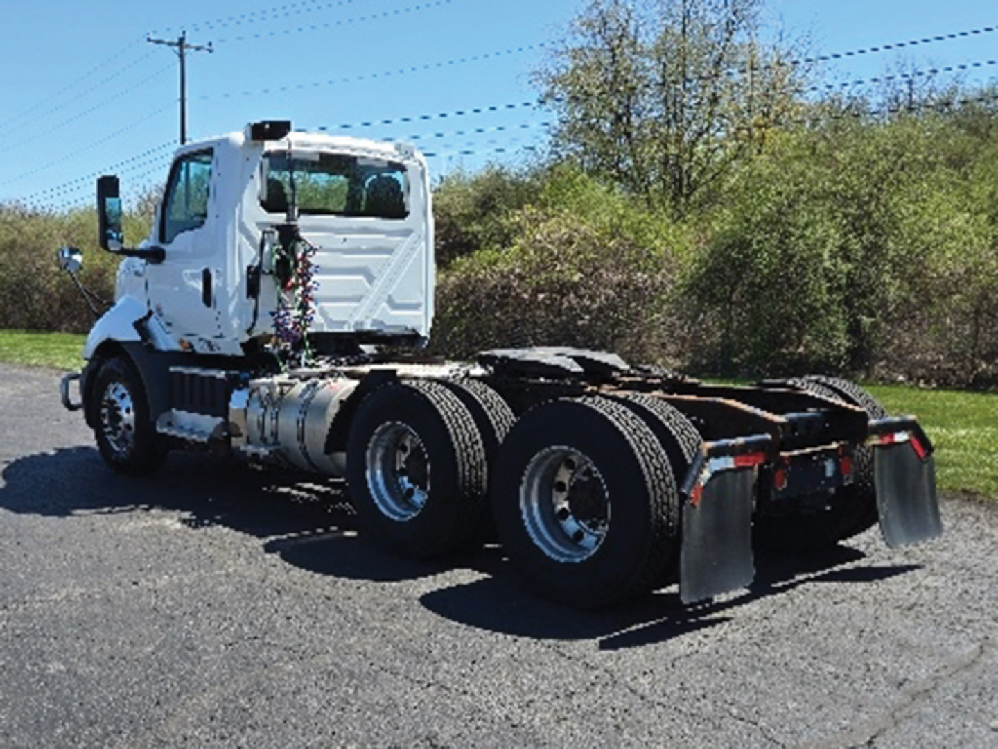 Truck chassis view showing white cab and dual rear axles with fifth wheel and mud flaps, no cargo, on pavement.
