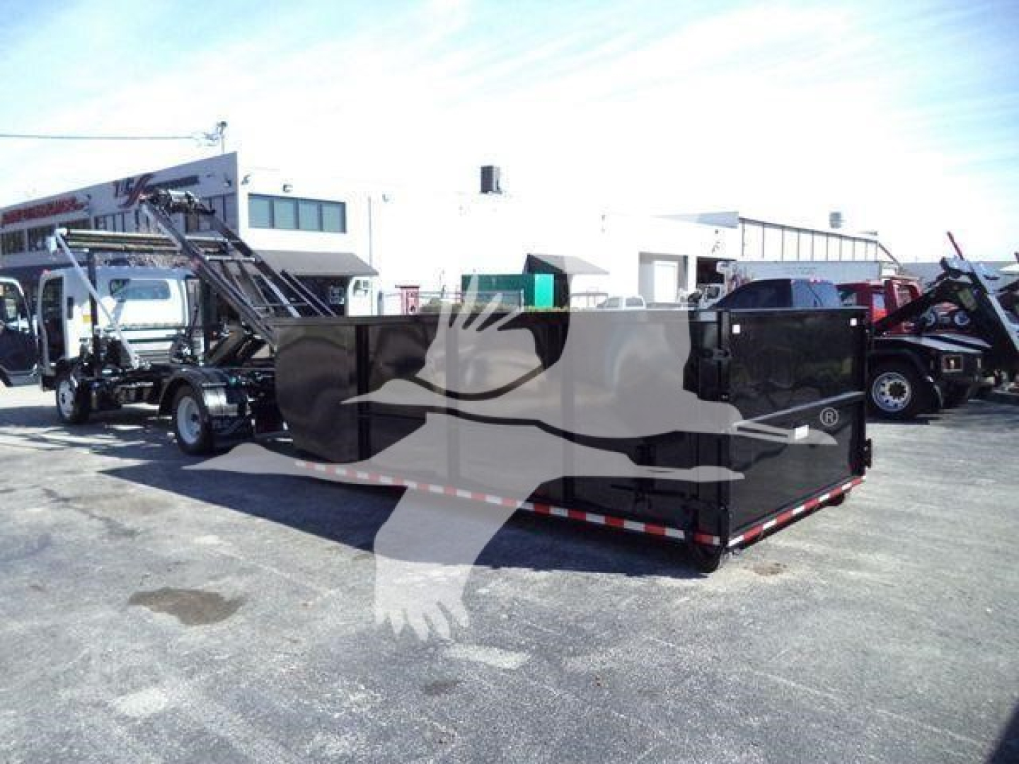 Isuzu NPR/NRR roll-off truck with large black dump bed in a dealership lot.