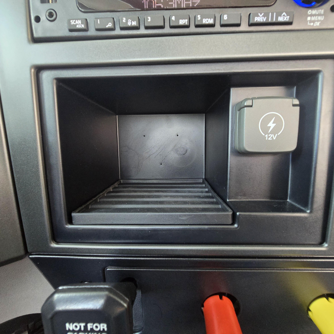 Cab interior showing 12V auxiliary power socket and open storage compartment in a Mack PI64T truck dash.