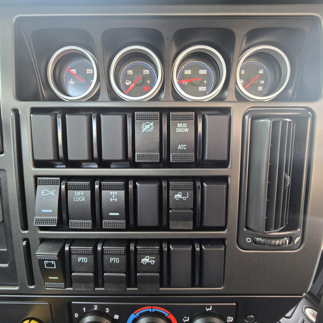 Dashboard gauges and control switches in a Mack truck cab showing multiple round gauges with blue/red needles, labeled buttons including MUD SNOW, ATC, DIFF LOCK, PTO, and a vertical vent on the right side.