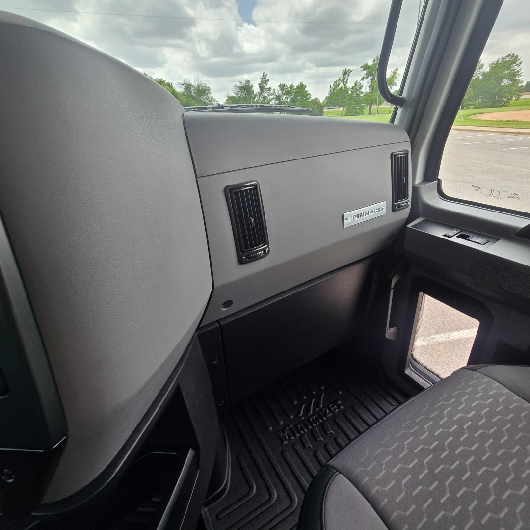 Dashboard and passenger side of a 2027 Mack PI64T truck cab interior showing glove compartment, air vents, and door window controls.