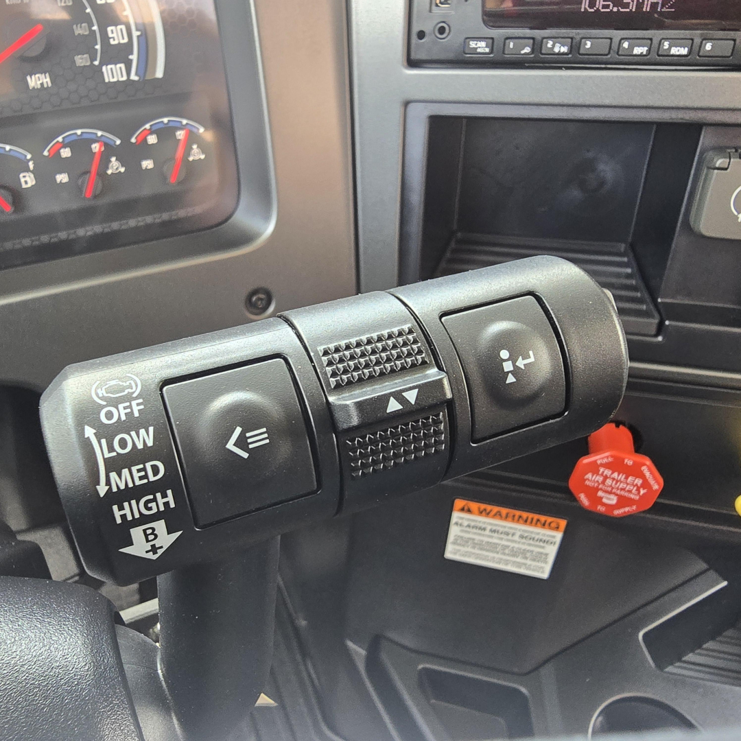 Steering column stalks with cruise control and turn signal lever, Mack PI64T dashboard area including warning label and red pull cap.