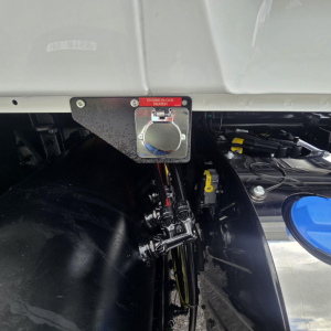 Mack PI64T engine bay area showing fuel/engine components and control fittings near the cab with a blue-cap reservoir