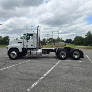 Side view of a white 2027 Mack PI64T truck with a chassis cab and triple axles, in a parking lot.
