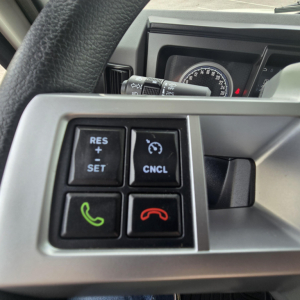 Steering wheel controls on a Mack PI64T truck dashboard showing cruise control buttons and phone/hang-up buttons.
