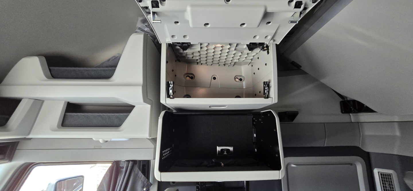 Cab interior View of Volvo VNL under-cab storage compartments with metal brackets and black bin, ceiling area visible.