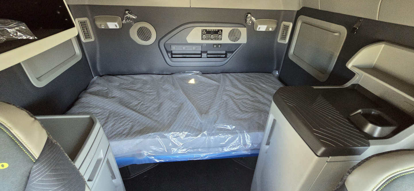 Truck sleeper cabin with bed in the back, storage compartments on sides, control panel and vents visible. Text on console reads Volvo logo and various controls.