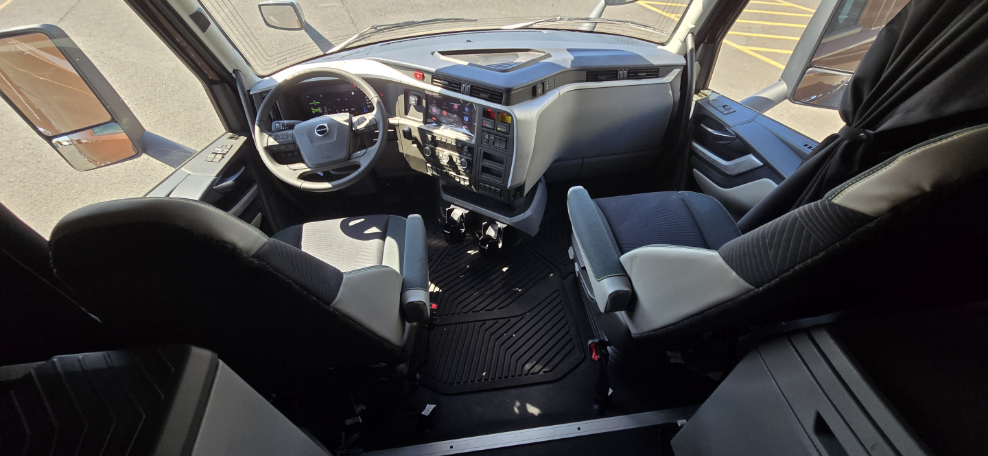 Volvo VNL cab interior showing driver's seat, dashboard with steering wheel, and passenger seat in a new conventional sleeper truck.