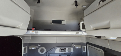 Cab interior of a Volvo VNL truck sleeper area with overhead storage compartments and a control panel, showing a small digital display and vents.