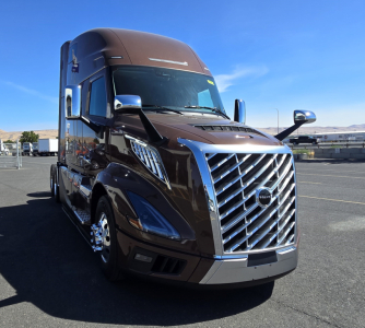 Volvo VNL64T860 truck at an angle showing the chrome grille, headlights, and side mirrors; brown exterior with some text on the hood and chrome accents.