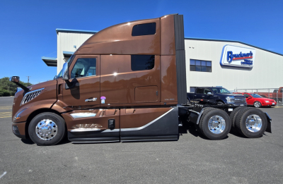 Volvo truck cab in brown with sleeper bunk and chrome wheels, side view, attached trailer package in lot.