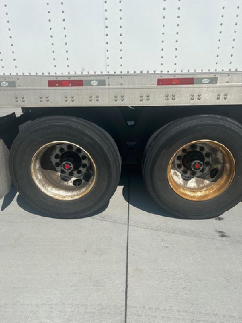 Trailer wheels and dual tires on the side of a utility van, showing two rims with visible bolts and hubcaps.