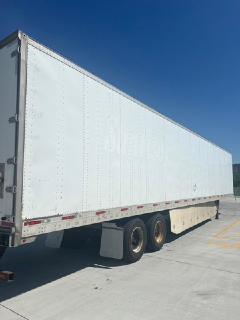 Trailer side view showing white box trailer with two rear axles and wheel wells, no visible branding or text readable on side.