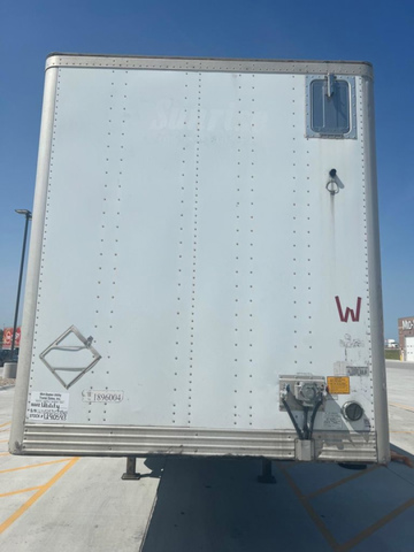 Rear view of a white utility trailer with riveted metal sides, small window near top-right, rear door handles, and various stickers/warnings near bottom edge.