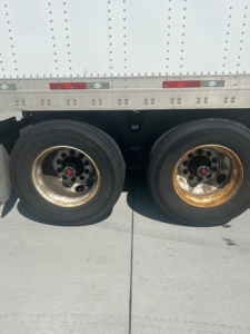 Trailer wheels and dual tires on the side of a utility van, showing two rims with visible bolts and hubcaps.