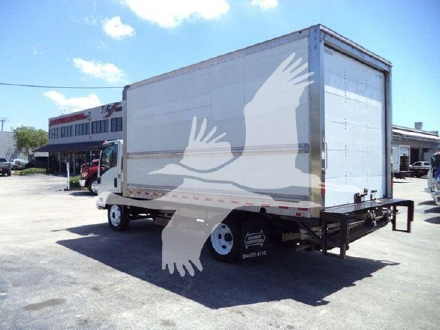 Isuzu NPR-HD box truck with white cargo box, side view showing rear and cab. Some branding on cab, no legible text visible on side.