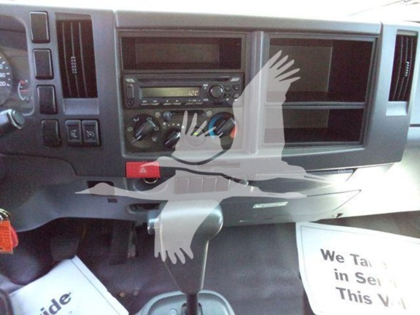 Isuzu NPR-HD dashboard view showing center console with radio, climate controls, and empty compartments; gear lever visible in foreground.