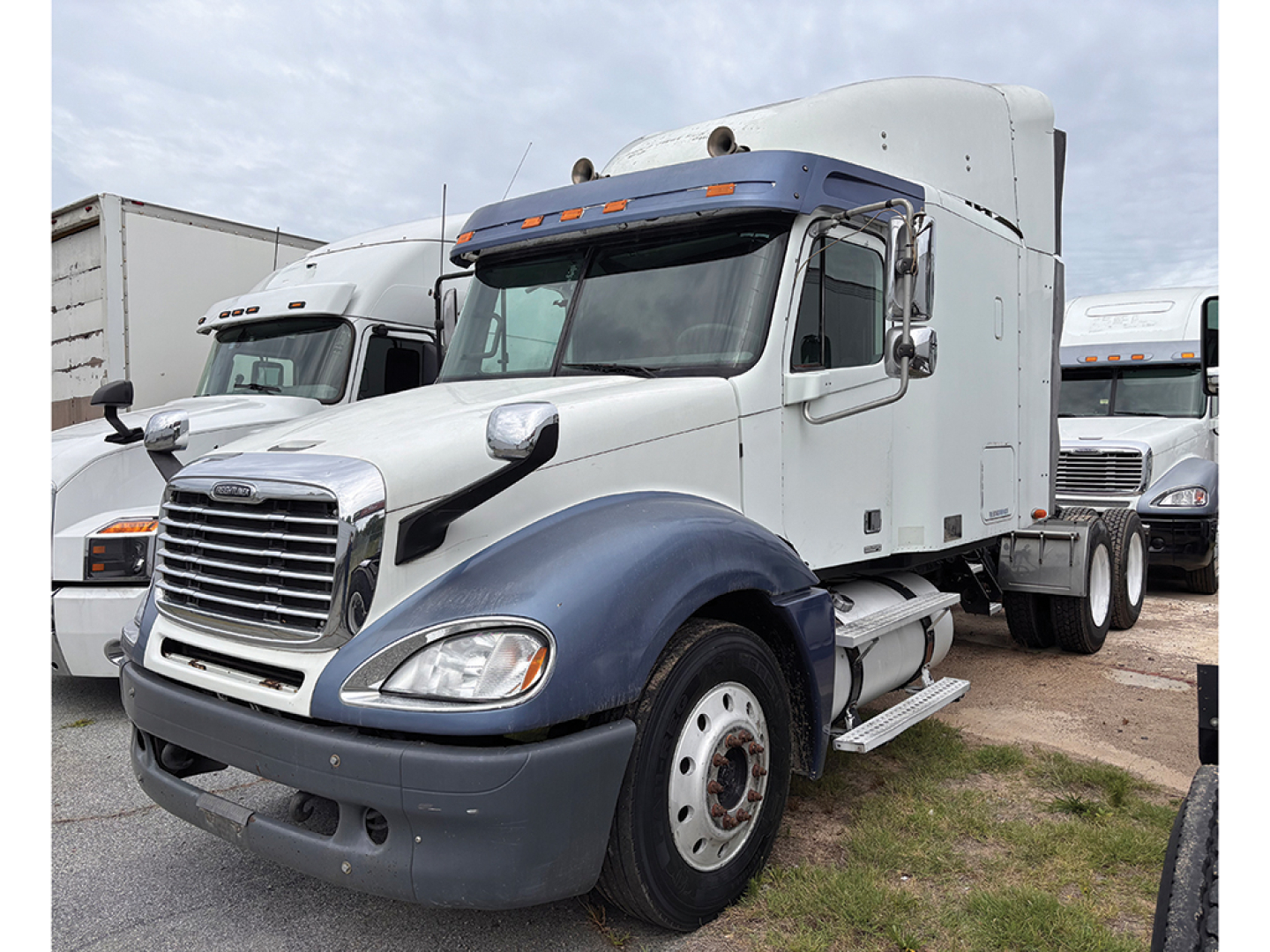 Truck shows a white Freightliner CL120 Columbia sleeper with blue fenders, front grille, and dual exhaust side panels. Vehicle text not legible.