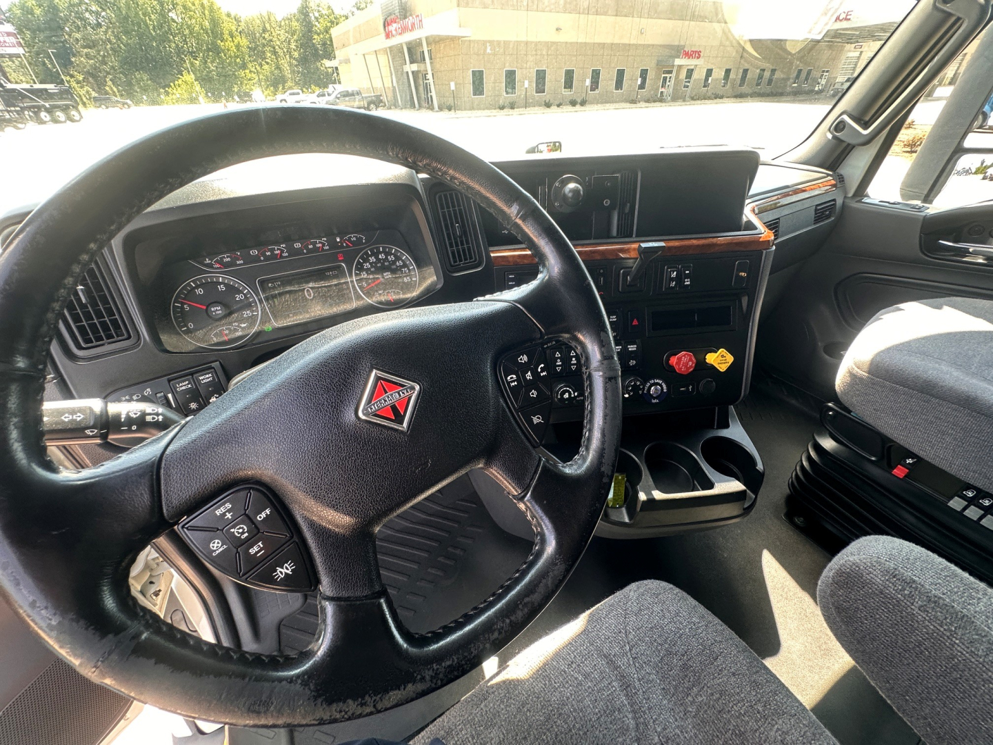 Truck cockpit showing steering wheel with Diamond/Vic emblem, dashboard gauges, center console with controls and cup holders; driver seat visible in a 2021 International LT625 interior.