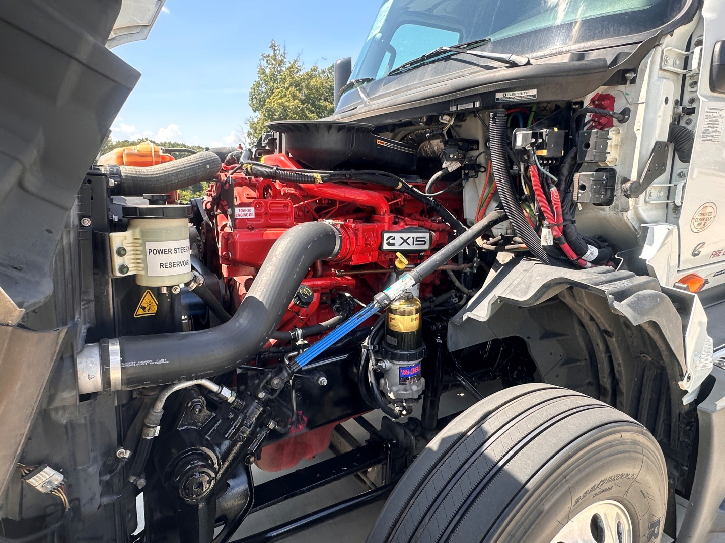 Truck engine bay of a 2021 International LT625 showing red engine and EXIS label, hoses, coolant reservoir, and exposed components.