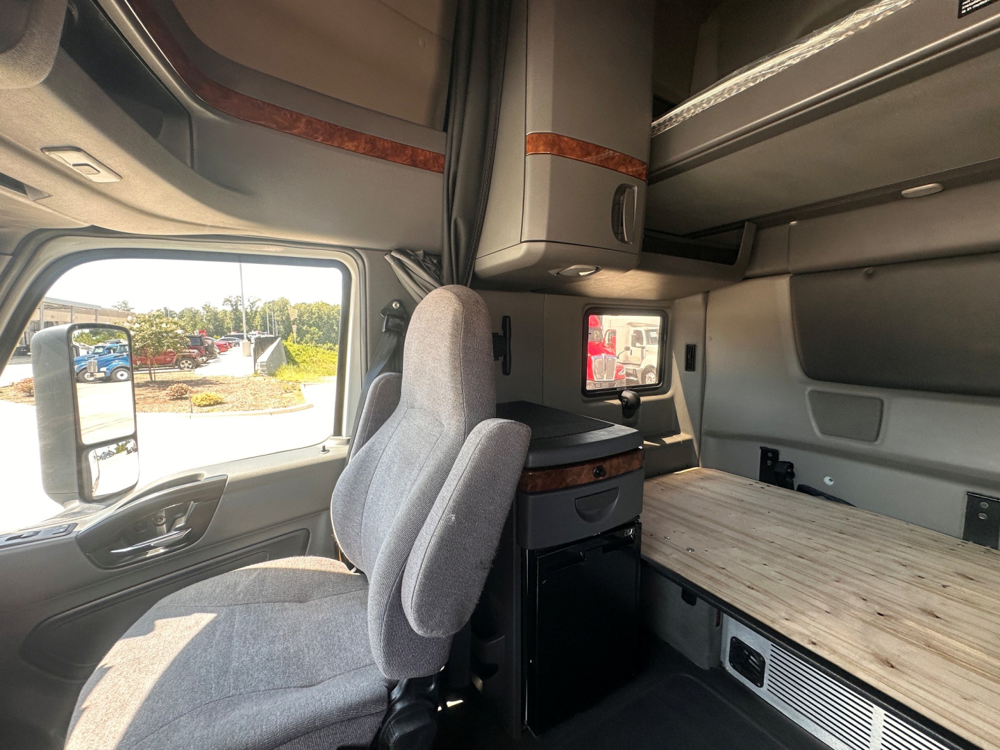 Interior of a 2021 International LT625 sleeper cab showing driver seat, upper cabinet, and a wooden sleeper desk surface with storage drawers.
