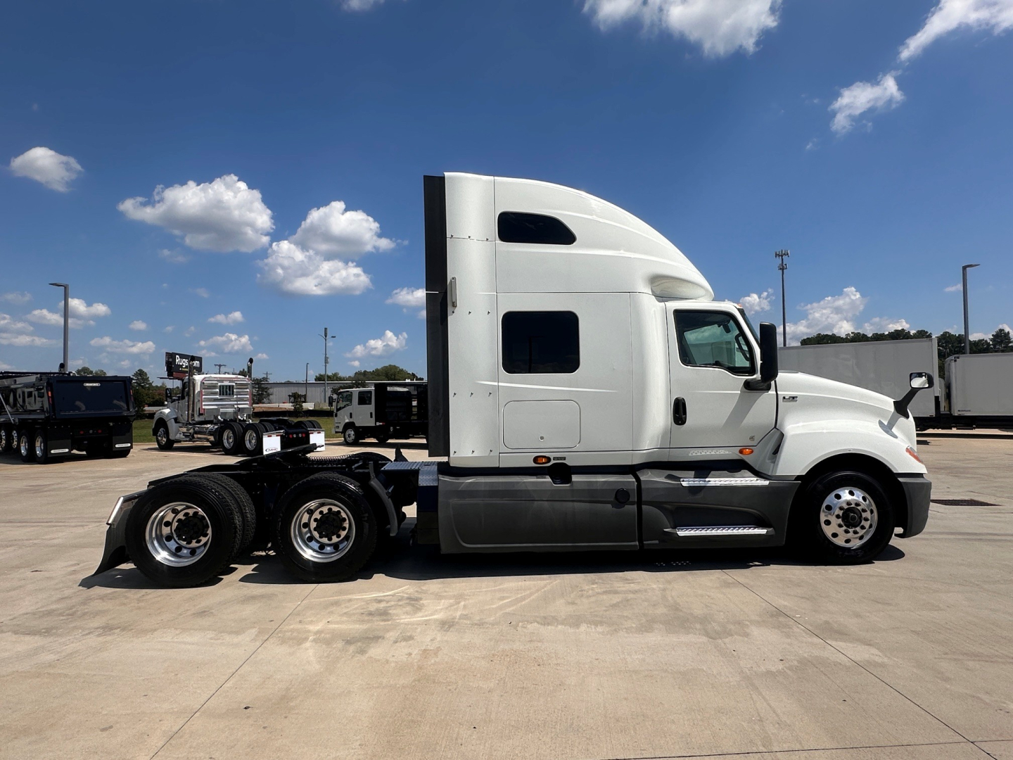 Truck cab and chassis of a 2021 International LT625 in a dealership lot, side view showing sleeper cab and rear axles.