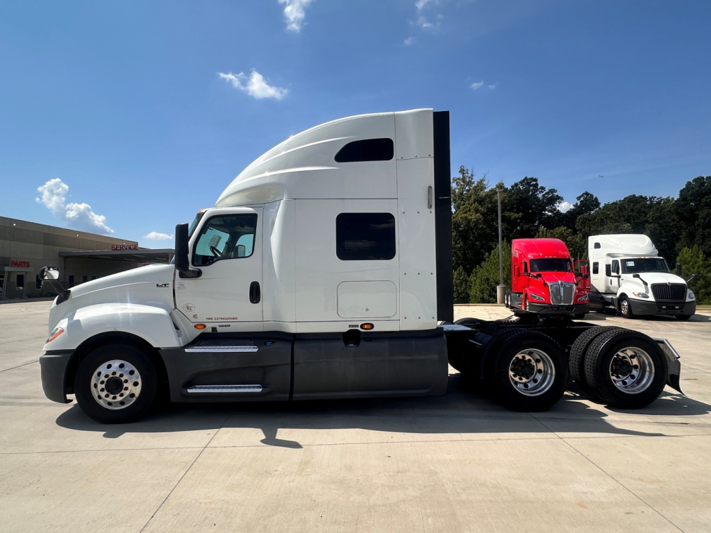Truck cab of a 2021 International LT625 in a side profile view with a white cab and red and white trucks in the background.