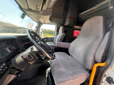 Interior cab view of a 2021 International LT625 truck showing steering wheel, dashboard, driver and passenger seats, and a lower bunk in sleeper compartment.