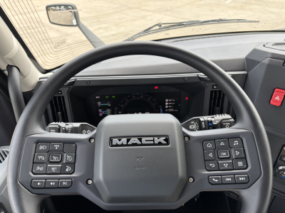 Truck steering wheel with MACK logo center, dashboard and instrument cluster visible in a Mack AN64 cab interior.
