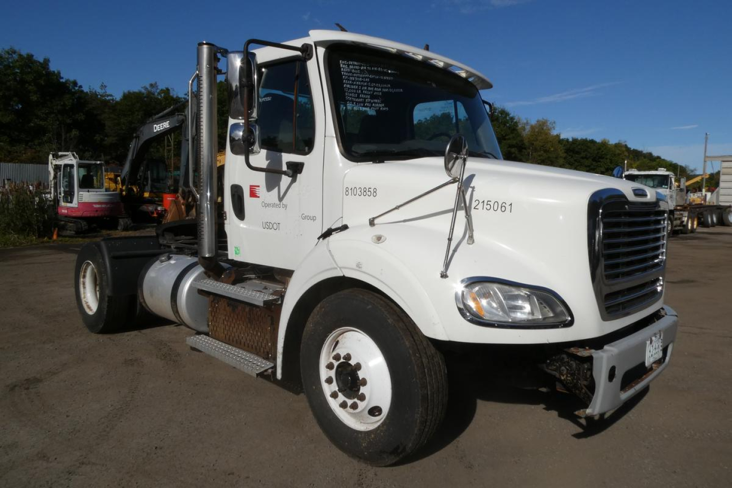 Truck cab side view showing Freightliner M2 112 with white exterior, chrome exhaust stacks, and front bumper; window text and stock number visible.