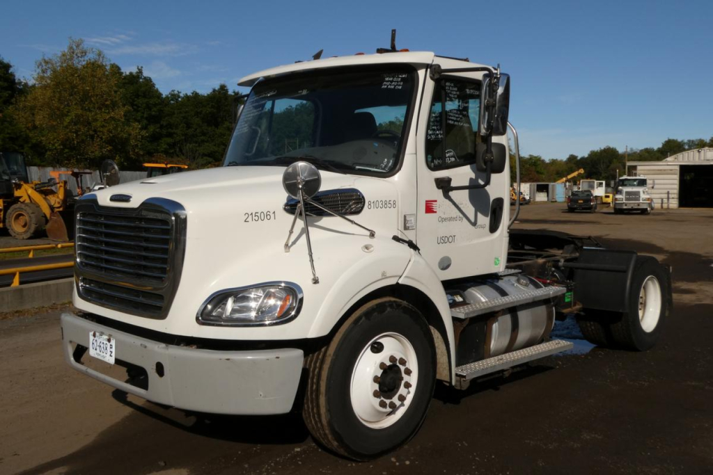 Freightliner M2 112 medium duty truck front-left view showing cab and chassis with headlights, mirrors, and steps.
