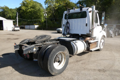 Truck chassis and cab of a 2015 Freightliner M2 112 Daycab from rear-left view showing fifth wheel and dual rear tires.