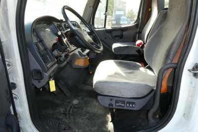 Truck cab interior of a 2015 Freightliner M2 112 daycab showing steering wheel, dashboard, driver seat with controls, and pedals.