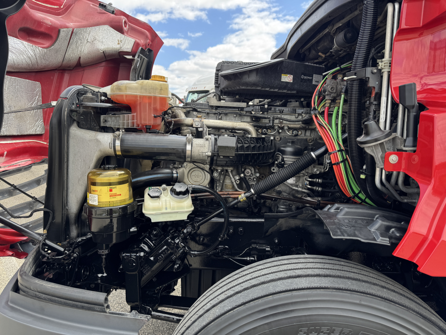 Truck engine bay of a 2019 Freightliner Cascadia 126 showing various components including coolant reservoir, oil filter, hoses, wiring, and engine block.