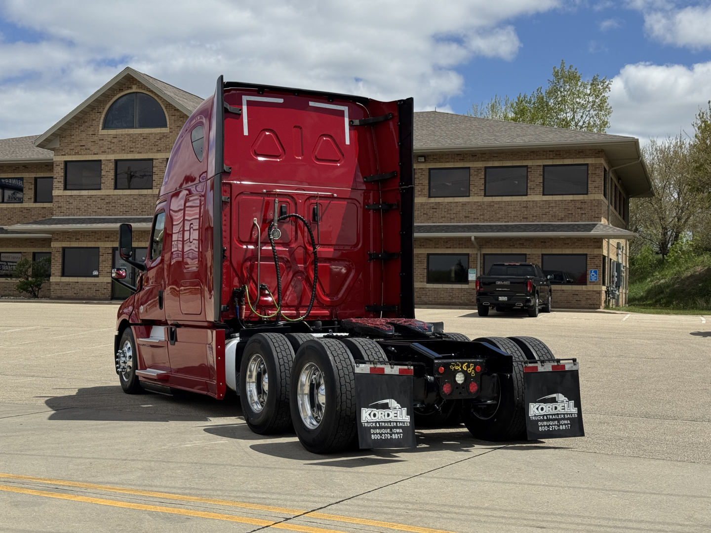 Truck rear view of red Freightliner Cascadia 126 tractor in a parking lot, showing back of cab, dual rear axles, and fifth-wheel area.