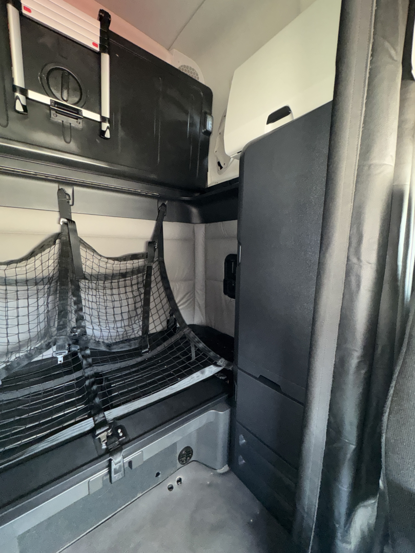 Freightliner Cascadia sleeper cab interior showing storage net, shelves, and cabin partition.