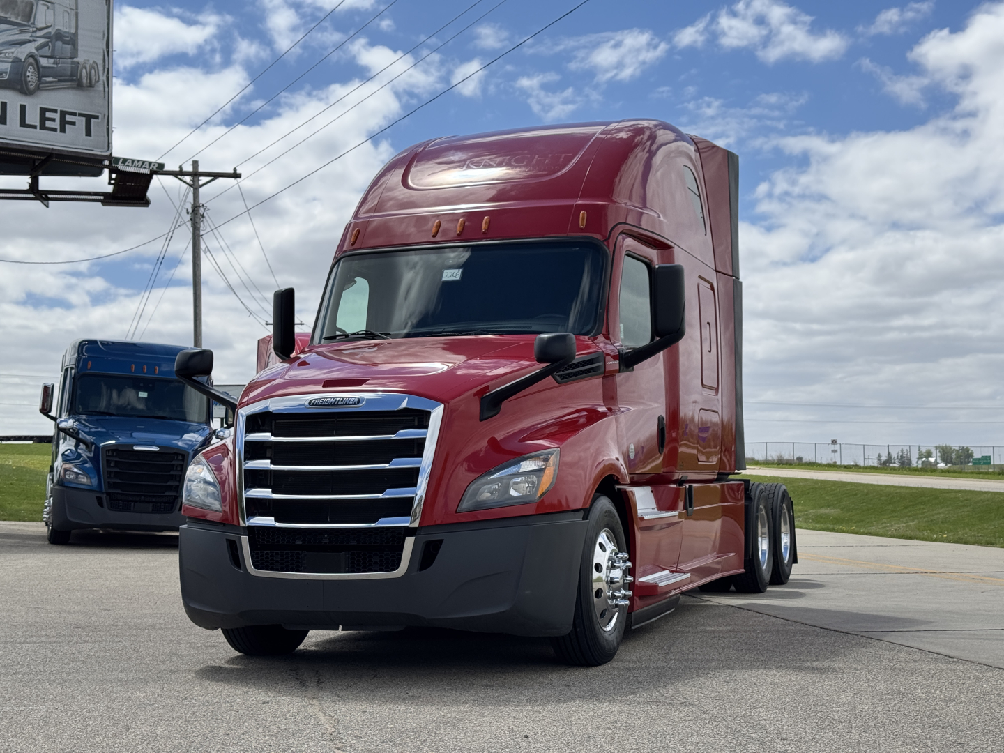 Truck image: red 2019 Freightliner Cascadia 126 semi, front three-quarter view, with sleeper cab, black bumper, chrome grille, two mirrors, blue sky