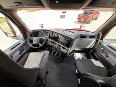 Freightliner Cascadia cab interior showing steering wheel, dashboard controls, center console, and front seats.