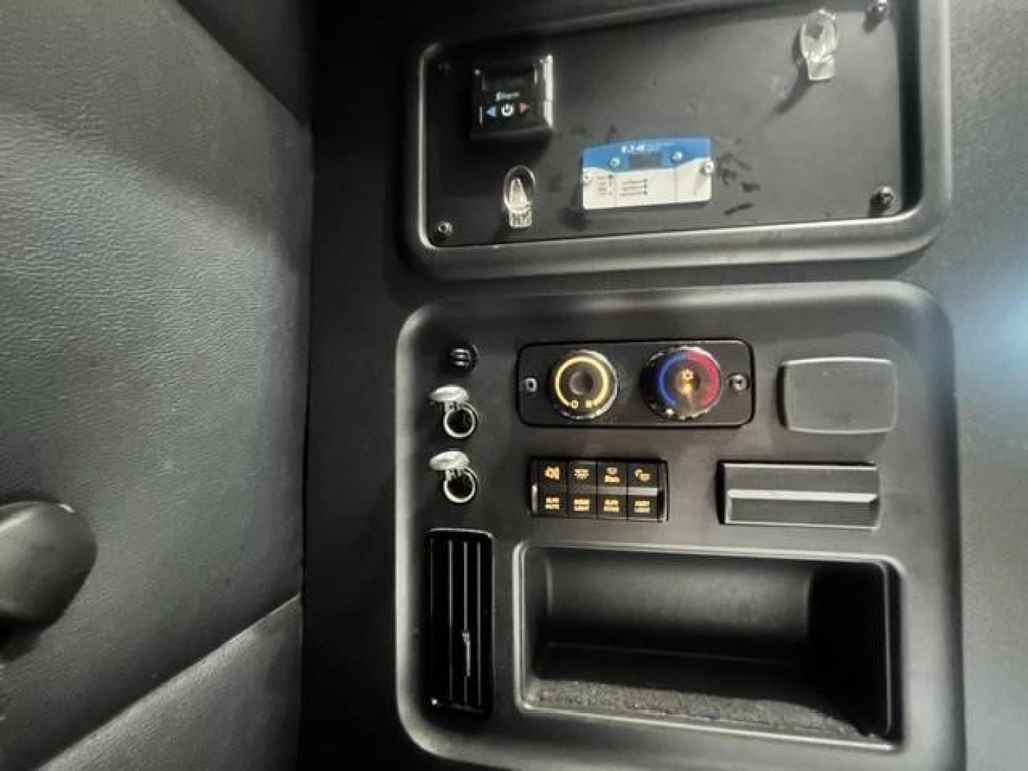 Freightliner Cascadia 126 dash area showing control panel with two round knobs and a selector switch, USB-like ports and a small storage slot.