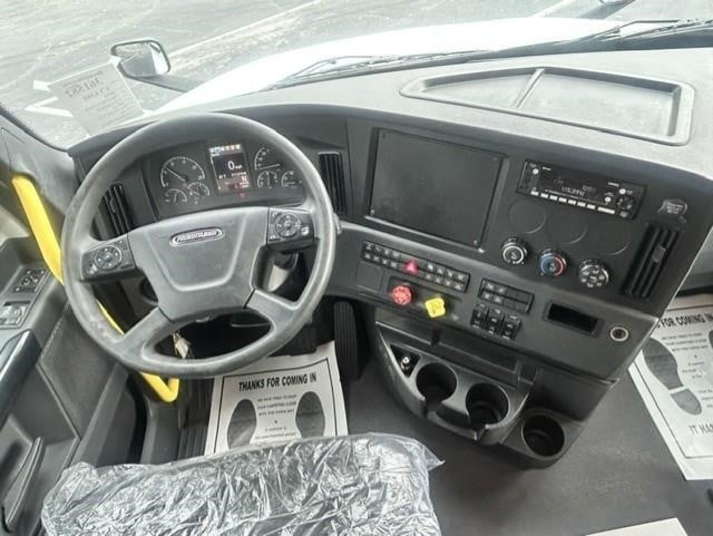 Dashboard and steering wheel of a 2024 Freightliner Cascadia 126 tractor showing digital gauges, center console, steering wheel with controls, and cup holders.