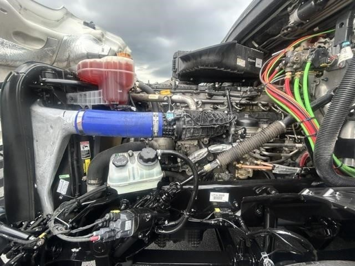 Truck engine bay with various hoses and wiring; blue silicone hose connected to intercooler; fluid reservoir with green cap; exposed engine components and electrical harnesses.