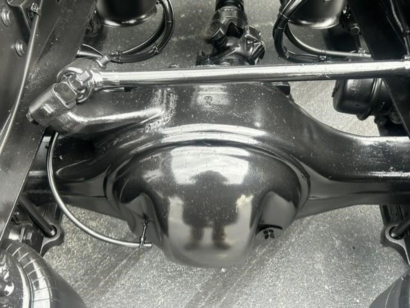 Rear axle housing and suspension components of a Freightliner Cascadia 126 drivetrain showing solid axle and differential housing with linkage rods and black painted metal surface.