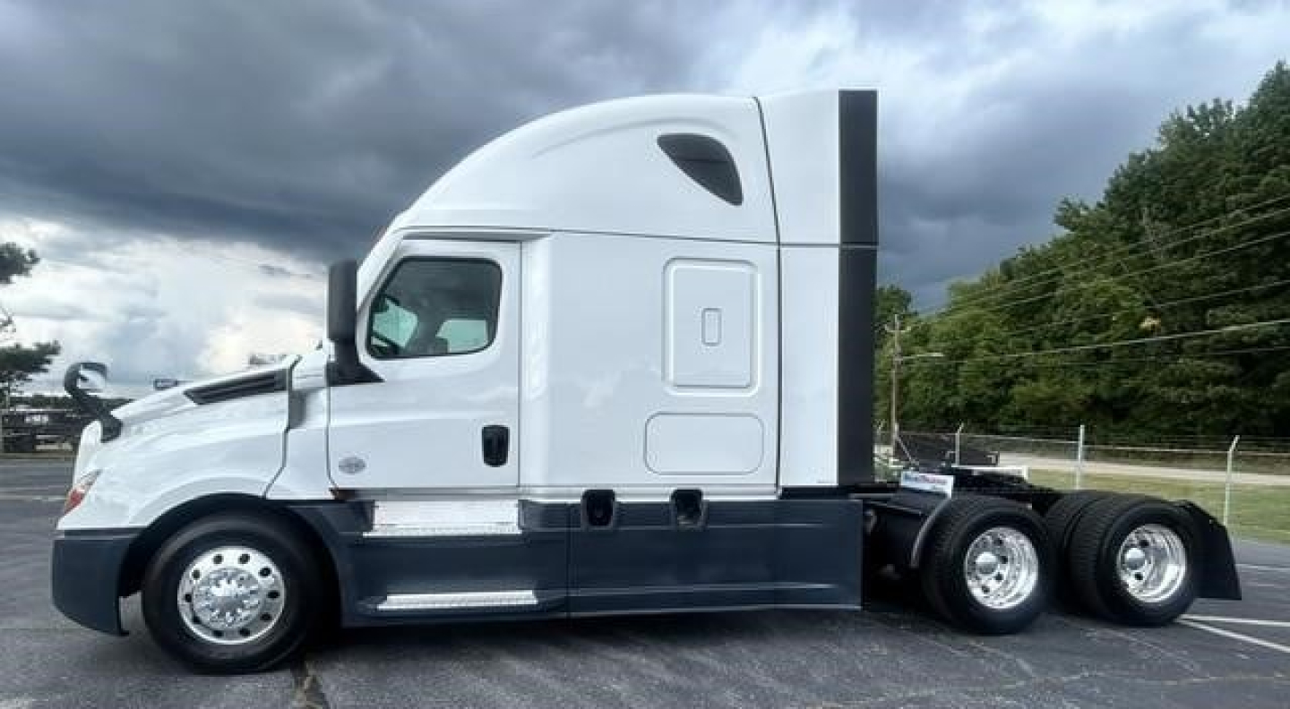 Truck side view showing a 2024 Freightliner Cascadia 126 sleeper cab with white and dark blue accents, three-axle rear setup, and streamlined cab profile.