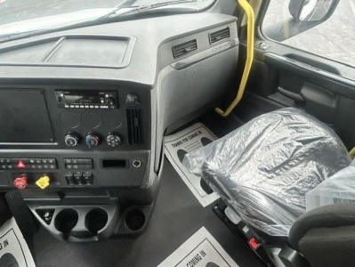 Cab interior of a Freightliner Cascadia 126 truck showing dashboard controls, radio slot, climate knobs, cup holders, and plastic-wrapped driver seat.
