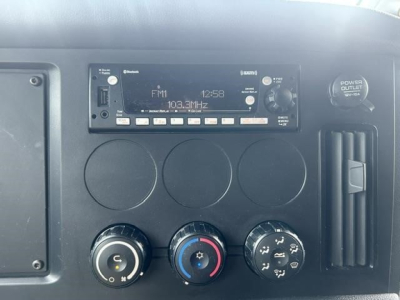 Dashboard panel of a Freightliner Cascadia 126 truck showing radio display, climate control knobs, and power outlet area.