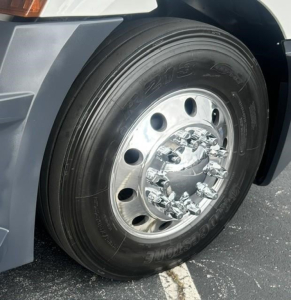 Truck wheel close-up showing aluminum rim with multiple lug nuts and Goodyear tire on Freightliner Cascadia 126 front axle.