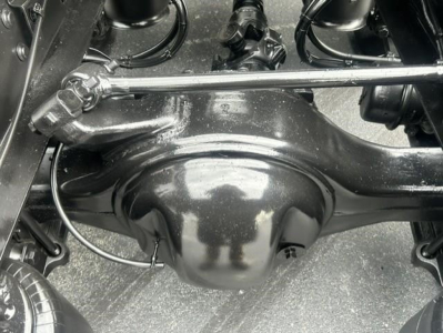 Rear axle housing and suspension components of a Freightliner Cascadia 126 drivetrain showing solid axle and differential housing with linkage rods and black painted metal surface.