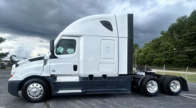 Truck side view showing a 2024 Freightliner Cascadia 126 sleeper cab with white and dark blue accents, three-axle rear setup, and streamlined cab profile.