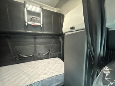 Cab interior of a Freightliner Cascadia sleeper showing storage box and mattress area.